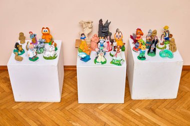 Galeri ortamında beyaz stantlarda sergilenen renkli kil heykelcikler. 28 Aralık 2023, Balti Moldova.