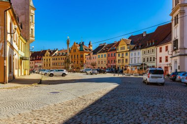 Güneşli bir günde renkli binaları ve klasik arabaları olan tarihi kaldırım taşı meydanı. 18 Mart 2025, Madalyon, Çek Cumhuriyeti.
