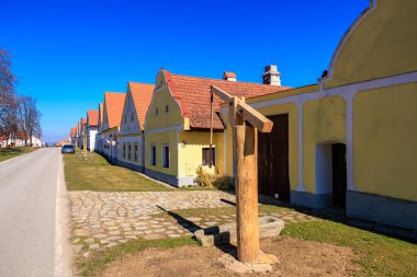 Kırsal kesimdeki mavi gökyüzünün altında tarihi sarı çiftlik evleri. 21 Mart 2025, Holasovice, Çek.