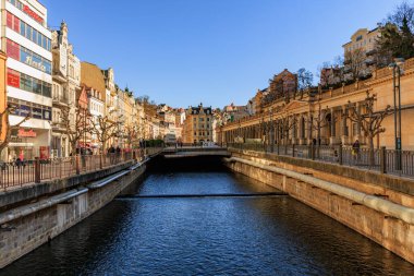 Karlovy 'de güneşli bir günde manzaralı nehir ve tarihi mimari çeşitlilik gösterir. 18 Mart 2025, Karlovy Vary, Çek Cumhuriyeti.