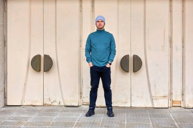 Adam modern, minimalist kapıların önünde kendinden emin duruyor. Elleri tesadüfen cebinde duruyor. O bir deniz mavisi süveteri ve koyu renk pantolon giyer. Bej kapılar dairesel kollara sahiptir.