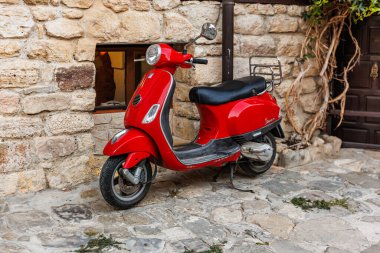 Kırmızı Vespa scooter 'ı, sarmaşık sarmaşıklı taştan duvarın önüne park etmiş. 1 Ağustos 2025, Nessebar Bulgaristan.