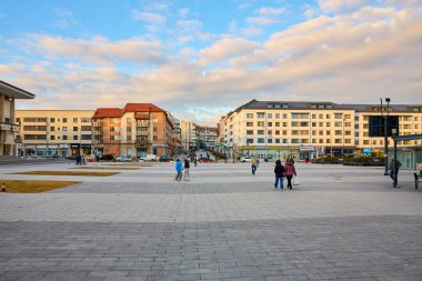 Şehir meydanında yayalar ve günbatımında modern binalar. 3 Mart 2026, Suceava Romanya.