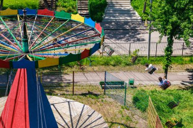 Güneşli parktaki boş renkli salıncak manzarası. Yanında iki kişi var. 22 Mayıs 2025 Balti Moldova.