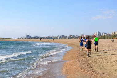 Sahilde okyanus kenarında koşan bir grup adam ve arka planda gökyüzü. 4 Mayıs 2025 Romanya.