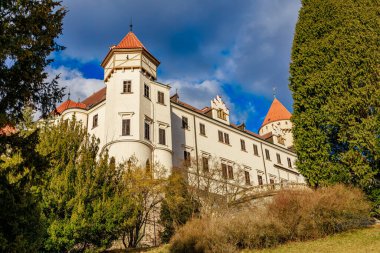 Mavi gökyüzünün altında yemyeşil yemyeşil, kırmızı çatı kuleleri olan görkemli Avrupa kalesi. 17 Mart 2025, Konopiste Şatosu, Çek Cumhuriyeti.