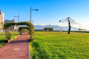 Günbatımında modern heykel ile manzaralı sahil parkı yolu. 4 Ağustos 2025 İzmir Türkiye.