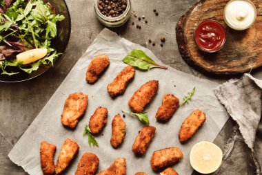 Ev yapımı tavuk nugget. Beyaz parşömen üzerinde külçeler. Ketçap ve mayonez. Kopyalama. Gri arka plan. Üst görünüm.