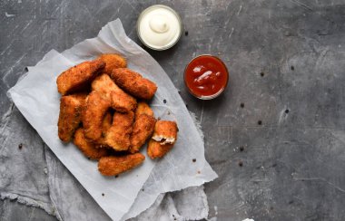 Ev yapımı tavuk nugget. Beyaz parşömen üzerinde külçeler. Ketçap ve mayonez. Kopyalama. Gri arka plan. Üst görünüm.