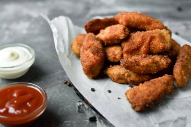 Ev yapımı tavuk nugget. Beyaz parşömen üzerinde külçeler. Ketçap ve mayonez. Kopyalama. Gri arkaplan.