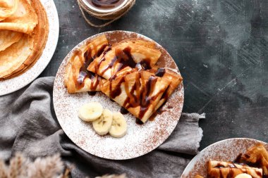 Güzel kahvaltı. Karamelli, çikolatalı ve muzlu ince krepler. Karanlık arka plan. Üst görünüm.