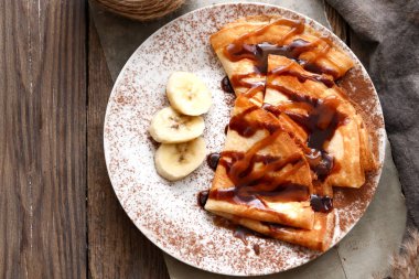 Güzel kahvaltı. Karamelli, çikolatalı ve muzlu ince krepler. Ahşap arka plan. Üst görünüm.