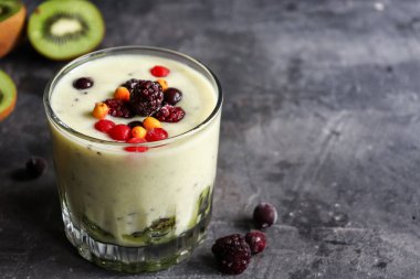 Böğürtlenli yoğurt ve bardakta kivi. Meyve ve meyve püresi. Kivili milkshake, ahududu, yabanmersini ve muzlu sağlıklı yiyecek. Koyu arkaplan.