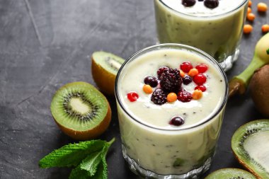 Böğürtlenli yoğurt ve bardakta kivi. Meyve ve meyve püresi. Kivili milkshake, ahududu, yabanmersini ve muzlu sağlıklı yiyecek. Koyu arkaplan.