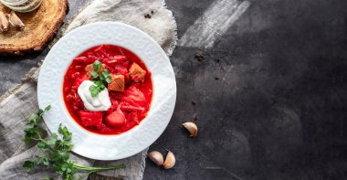 Red borsch with vegetables and meat in a white plate. Tomato soup. Dark background. Delicious healthy lunch.