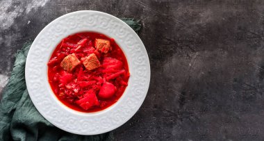 Red borsch with vegetables and meat in a white plate. Tomato soup. Dark background. Delicious healthy lunch.