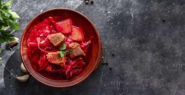 Red borsch with vegetables and meat in a clay plate. Steam from hot tomato soup. Dark background. Delicious healthy lunch. Top view. Copyspace