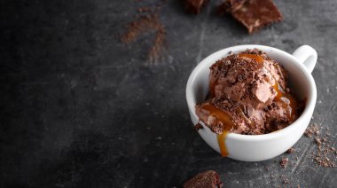 Çikolatalı hindistancevizli vejetaryen dondurmayı beyaz bardakta. Çikolatalı ve karamel kaplı dondurma topları. Koyu arkaplan, alanı kopyala.