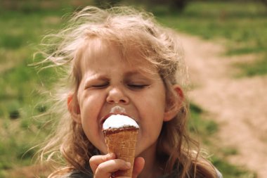 Doğadaki bir çocuğun portresi. Uzayı kopyala 4 yaşındaki güzel sarışın kız. Yeşil çimen arka planı. Çocuk soğuk dondurma yiyor..