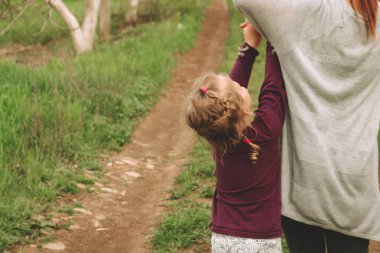 Anne ve kızı el ele tutuşuyorlar. Arkadan bak. Kız kardeşler el ele tutuşarak yürür. Doğadaki bir çocuğun portresi. Uzayı kopyala Güzel sarışın kız 4 yaşında..
