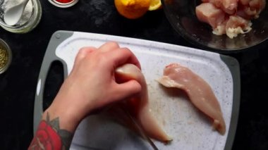 Slicing chicken fillet. Woman chef cuts chicken meat. Top view. Cooking process in the kitchen.