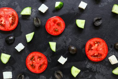 Sezar salatası malzemeleri. Dilimlenmiş domates, salatalık, peynir ve zeytin. Koyu arkaplanda taze sebzeler.