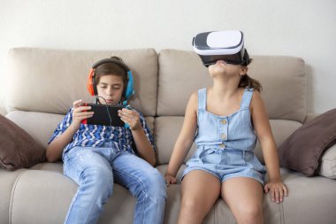 Genç bir çocuk ve küçük bir kız evdeki kanepede farklı dijital teknoloji cihazları kullanıyorlar..