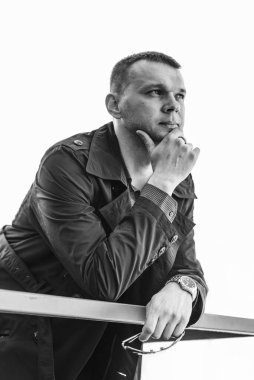 Paltolu ve gömlekli genç bir adam iskelede duruyor ve uzaklığa bakıyor. İş merkezinde genç ve yakışıklı bir iş adamı. Siyah beyaz fotoğraf.