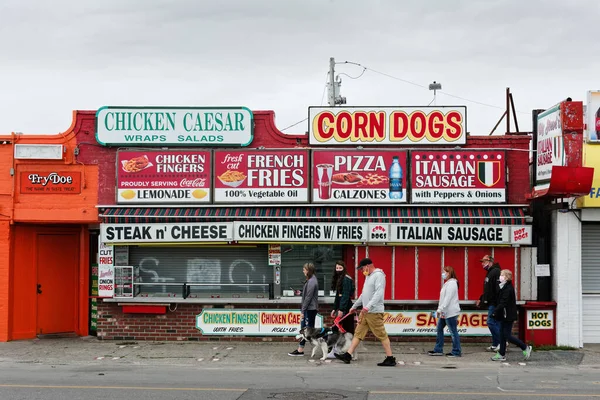 Tourists holding highlights map walk past one of many deserted vintage restaurants on the Hampton Beach, New Hampshire boardwalk. A normally packed tourist destination is now mostly desolate other than beach walkers and locals. — Stock Image Tourists Holding Highlights Map Walk One Many Deserted Vintage Restaurants Royalty Free Stock Photos