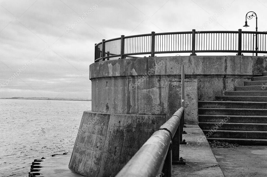 A concrete turret with stairs rising to an overcast sky along the Lynn Shore Reservation walking path above the sea wall. The scene was photographed during an usually high tide and rain showers. Lynn Shore Reservation is a protected coastal reservati