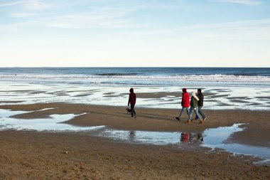 Hampton Beach State Park - Hampton, New Hampshire - Soğuk hava donanımlı dört ziyaretçi kışın sonlarında sahilde yürüyüş yapıyorlar..