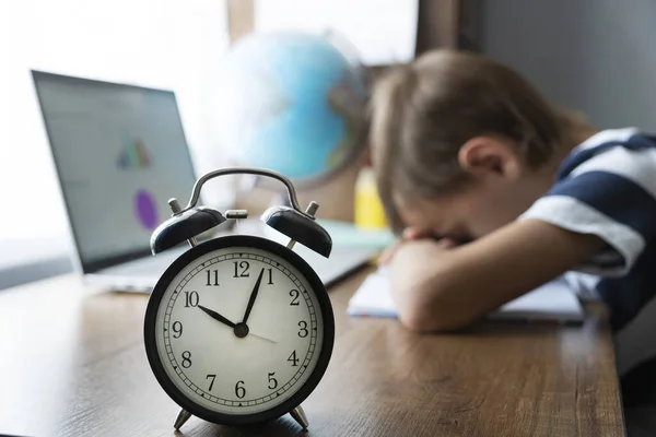 Odaklanamayan çocuk uzaktaki online matematik dersinde uyuyakalmış. Saat zamanı gösteriyor. E-öğrenme konusunda çok yorgun ve bitkinim. Ev uzaklığı öğrenme kavramı.