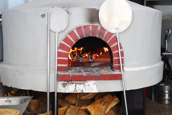 old authentic oven with round hearth with fire ready for cooking pizza in italian reastraunt. firewood is under the stove. pizza shovels stand near.