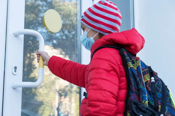 schoolboy in medical face mask pulls door before entering school. New reality, restrictions to prevent covid pandemic. Healthcare concept