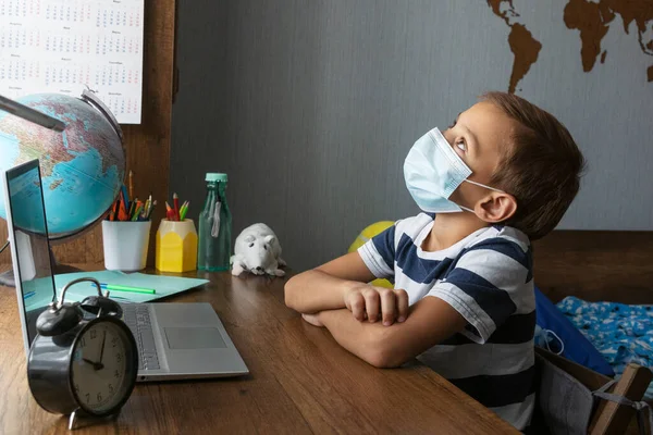 Tıp maskeli okul çocuğu öğretmeniyle çevrimiçi ders sırasında sıkılıyor ve tavana bakıyor. Çok zor uzak öğrenim