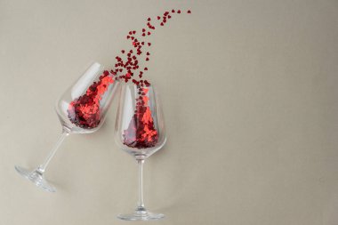 two wine glasses with little red heart sparkling confetti on light beige background, lots of copy space for text. Love and valentines day concept