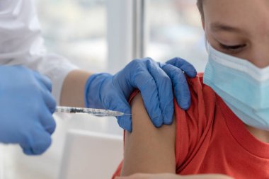 Aşı sırasında maske takan çocuk. Doktor iğne yapıyor. Çocuk korkmuyor ve doktorun bitirmesini beklemiyor. Aşılama kavramı.