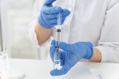 Kadın doktorlar mavi eldivenlerle aşı ampulünden şırıngayla sıvı ilaç alıyorlar. Aşılama kavramı