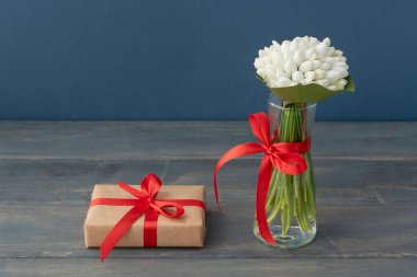 Küçük vazoda beyaz kar damlaları ve sarılı hediye kutusu ahşap ve mavi arka planda kırmızı kurdelelerle bezeli. Selamlar konsepti