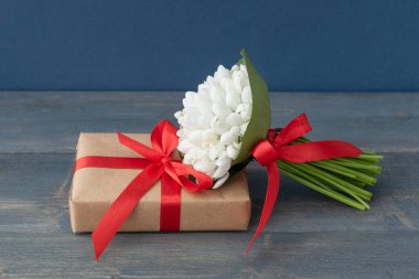 Küçük bir buket beyaz kar damlası kırmızı kurdeleyle kaplanmış tahta arka plandaki hediye kutusuna uzanıyor, metin için kopyalama alanı, selamlaşma konsepti.