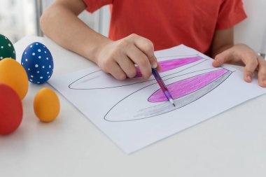 Paskalya bayramında erkekler el ele tutuşup tavşan kulağı boyuyor. Renkli yumurtalar beyaz masanın üzerinde. Paskalya kutlaması için hazırlıklar