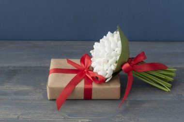 Selamlama konsepti, kırmızı kurdeleli beyaz kar damlaları koyu ahşap arka plandaki paketlenmiş hediye kutusunda uzanıyor, bir sürü kopyalanmış alan. İlk bahar çiçekleri