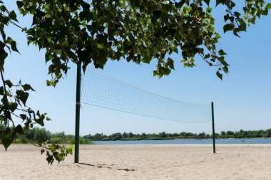Nehir kıyısındaki kumsalda voleybol ağı, aydınlık yaz günü. Açık hava aktiviteleri, sağlıklı yaşam tarzı konsepti