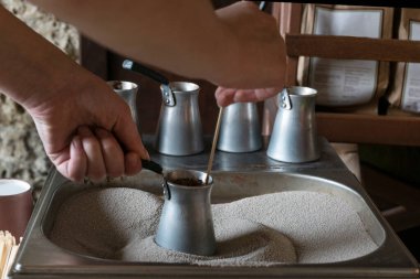 Geleneksel Türk kahvesini sıcak kumda hazırlarken kadının elleri metal Türk 'ü tutuyor. Odaklanamayan dört metal kap arkasında duruyor..