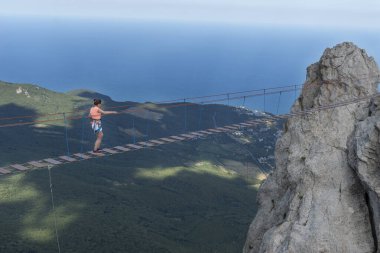 Genç bir kadın Ukrayna, Kırım 'daki Ai-Petri dağının zirvesinde uzun bir ip köprüden geçiyor. Dağlardaki macera sırasında cesur ve cesur olmak, aktif yaşam tarzı.