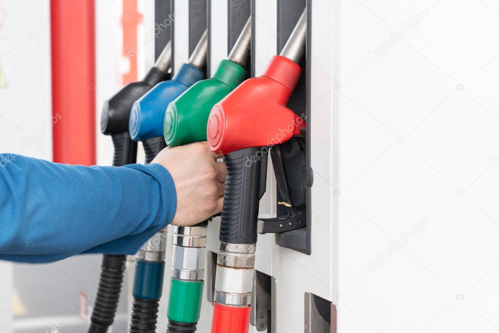 Man's hand preparing for refueling car and holding green handle of gas pump on gas station. Refueling car process.