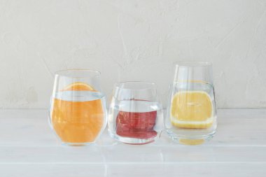 Distorted images of cutted lemon, orange and strawberry behind transparent glasses with water on light background, resreshing vitamin drink, creative images concept.