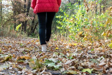 Woman is walking on footpath in autumn park, copy space. Active lifestyle, walking in beautiful places, changing of seasons.