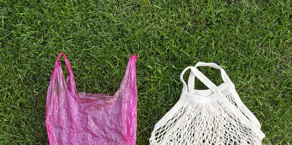 Comparison of eco mesh cotton bag and plastic shopping bag on green grass background, copy space, banner size. Zero waste concept.