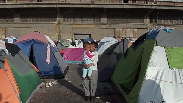 Сирийский мальчик с младшей сестрой на руках в палаточном лагере для беженцев — стоковое видео